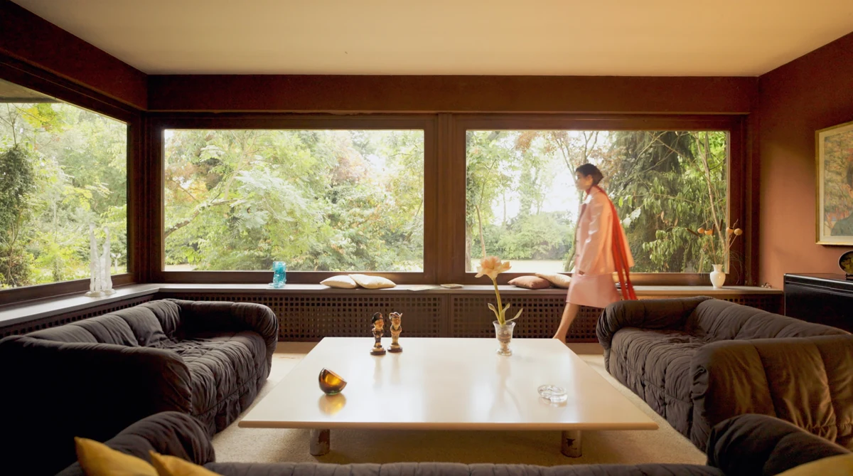 Model crossing a wood panelled living room in a pink Gucci coat, frame from the fashion film for MOJEH